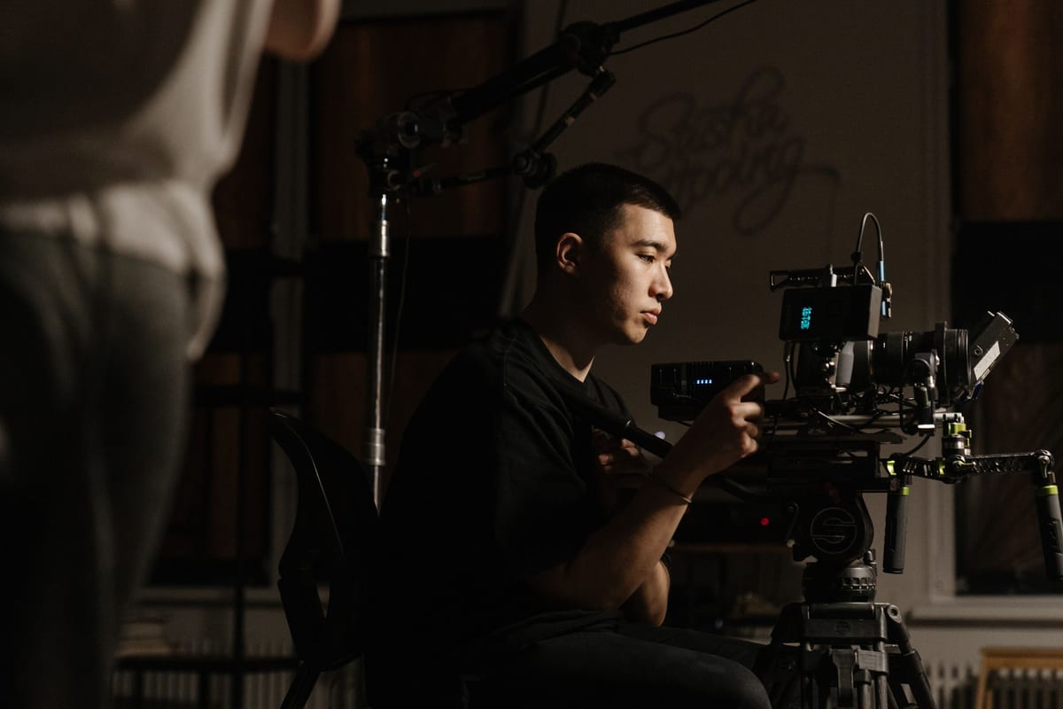 Side view of cameraman operating professional equipment during film production indoors.