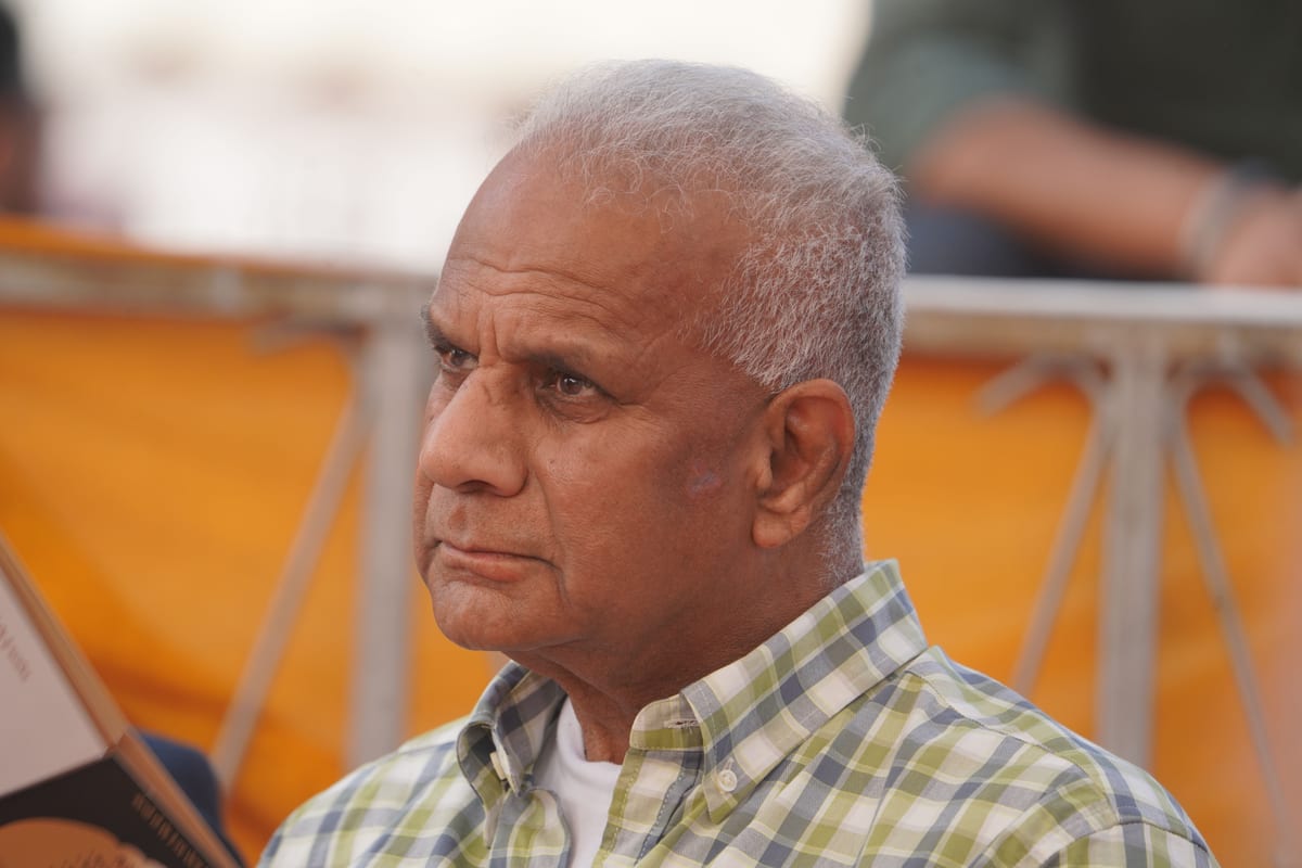 Elderly man in checkered shirt contemplating in an outdoor setting.
