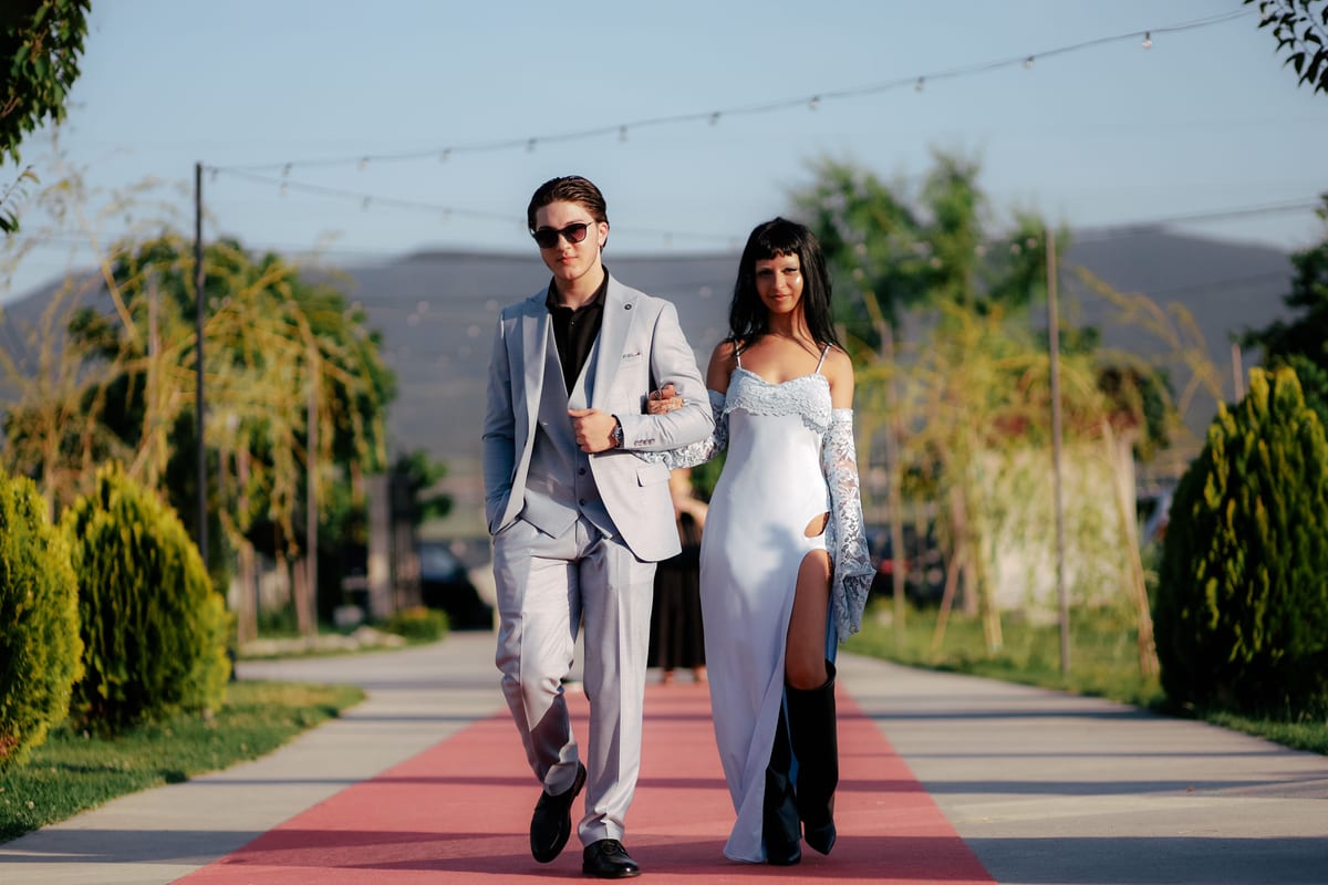 Stylish couple walking confidently on red carpet outdoors in elegant fashion.