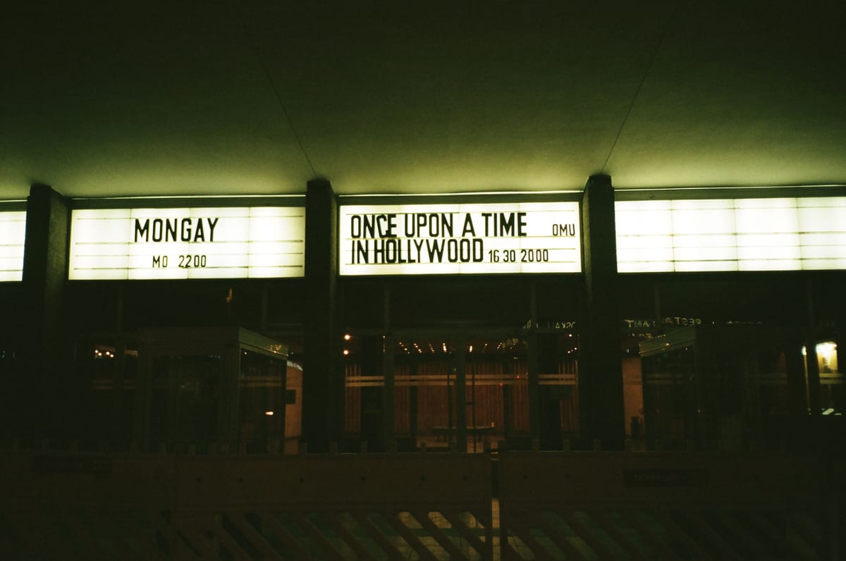 Outdoor view of an illuminated theater marquee displaying movie titles at night.
