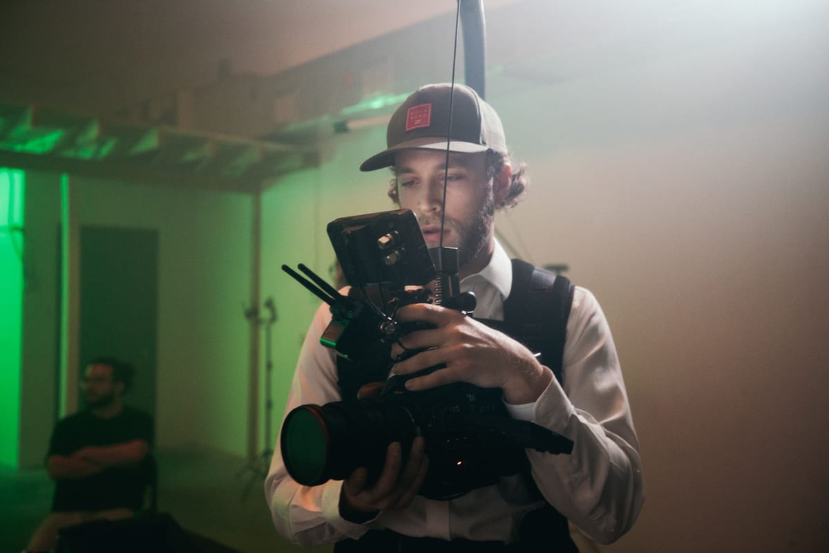 Videographer adjusting camera equipment on a film set indoors under dramatic lighting.