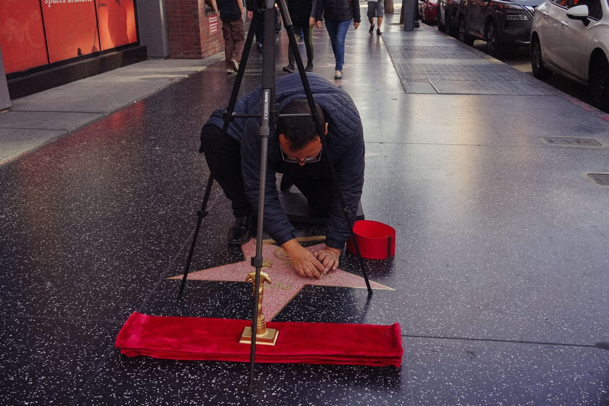 A man meticulously cleans a star on the Hollywood Walk of Fame, symbolizing celebrity culture.
