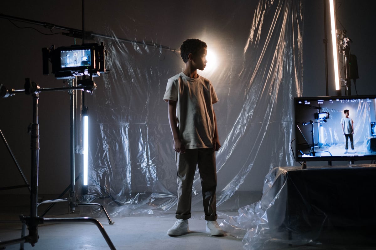 A young boy stands in a film studio surrounded by cameras and screens under soft lighting.