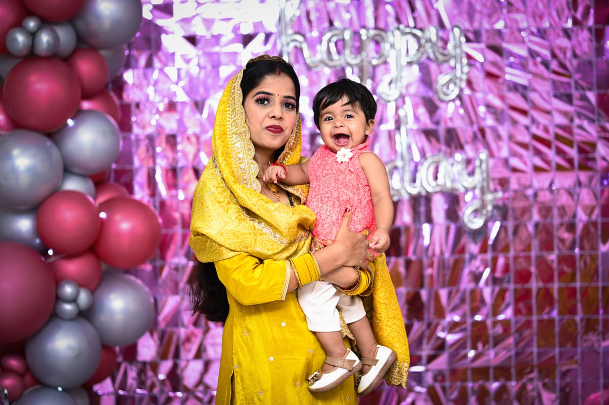 Portrait of a mother and daughter enjoying a birthday celebration with balloons and decorations indoors in India.