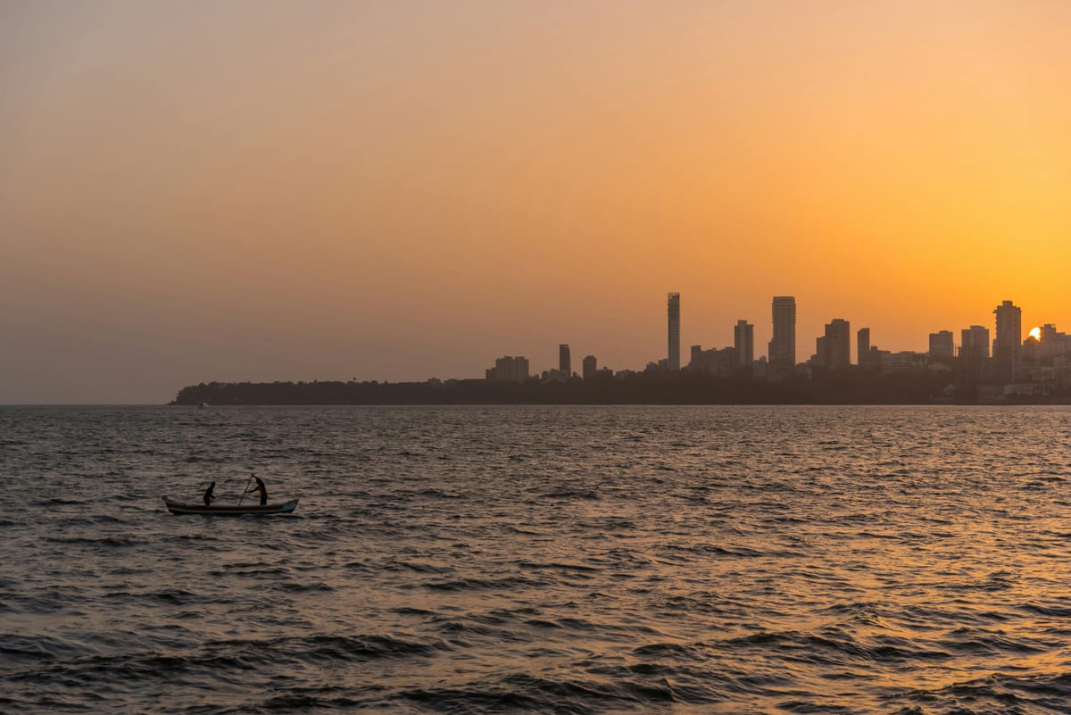 Silhouette of fishermen on a boat at sunset with a city skyline in the background.