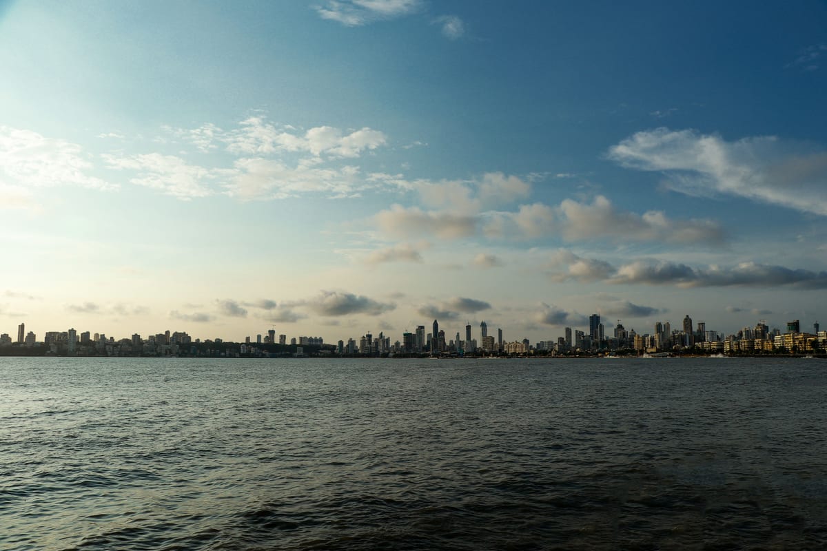 Panoramic view of Mumbai skyline with calm sea and cloudy sky in daylight.