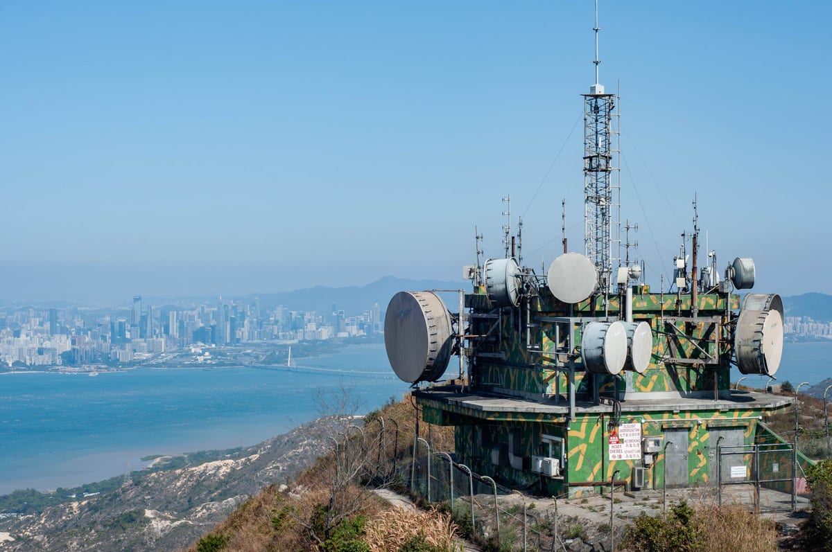 A telecommunications tower on a hill overlooking the Hong Kong city skyline and water.