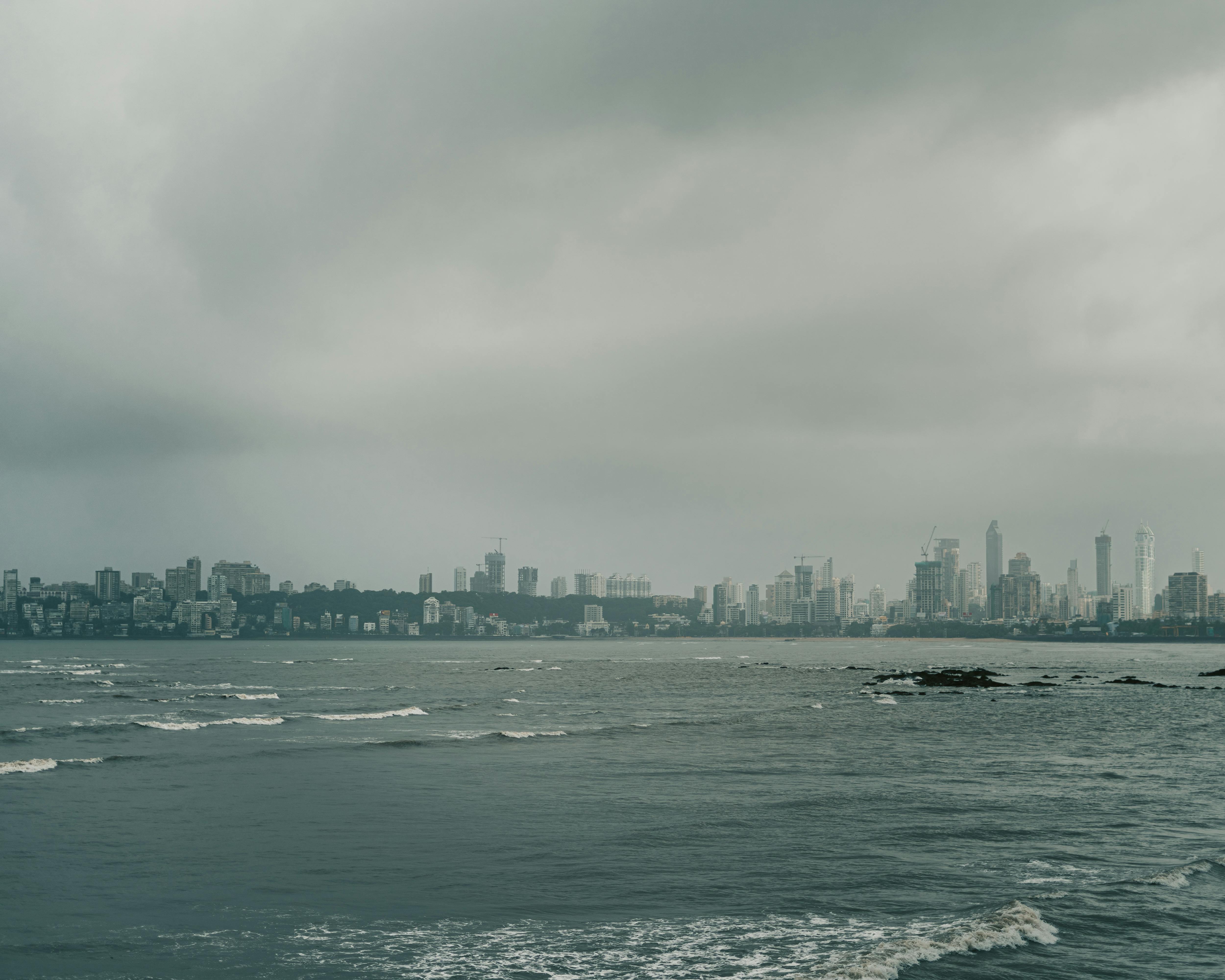 View of Mumbai's skyline under a cloudy sky, with the ocean foreground on an overcast day.