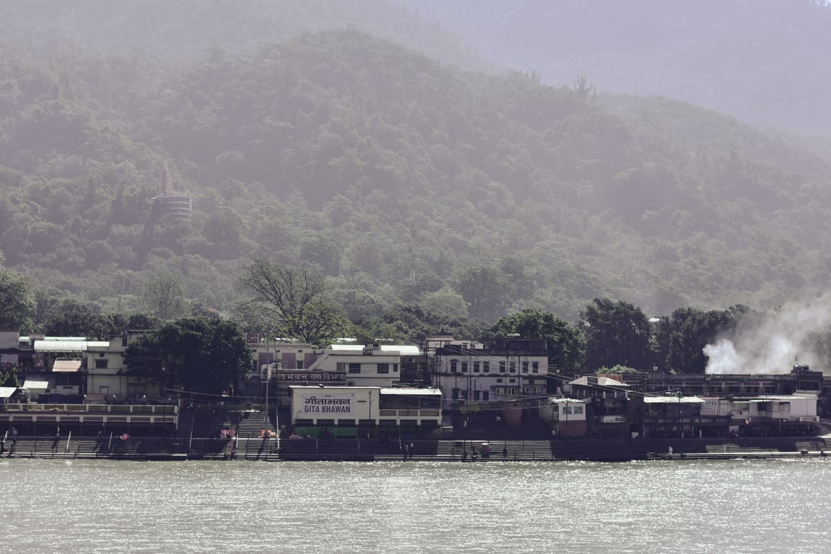View of a tranquil riverside village with dense green hills in the background, ideal for travel and nature scenes.