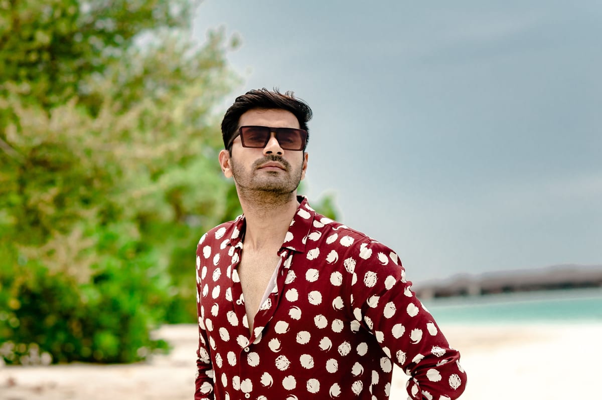 Fashionable man wearing sunglasses poses on a sunny Maldives beach.