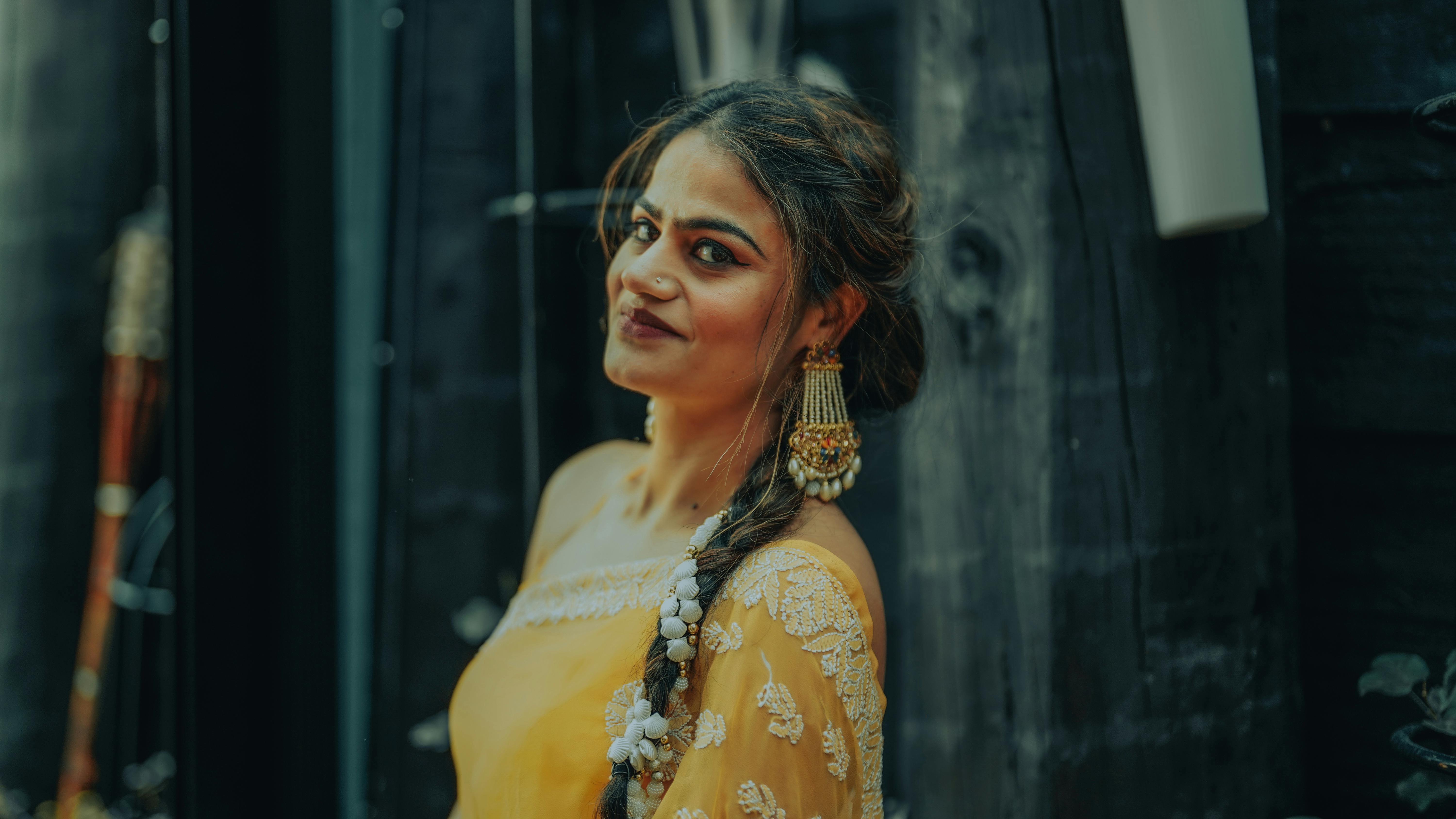 A smiling woman in a stylish yellow dress with embroidered details, standing outdoors in Auckland, New Zealand.
