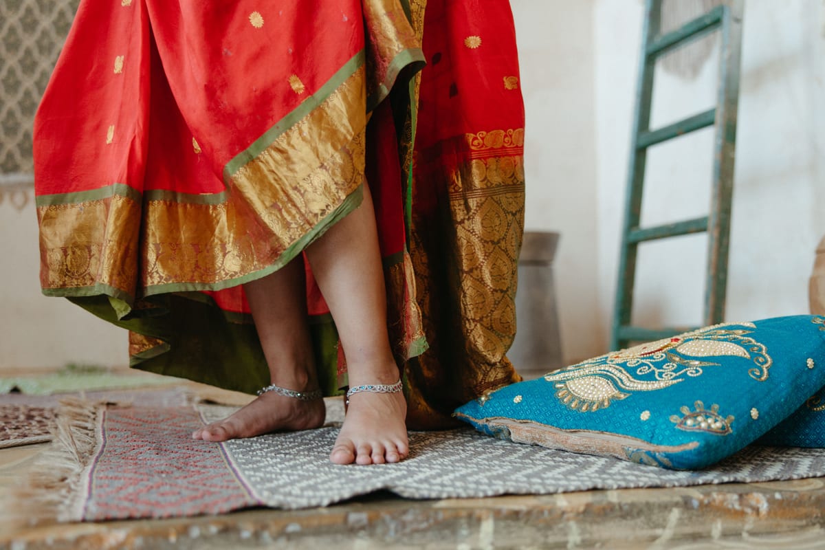 A woman in traditional clothing with anklets, standing on ornate carpets, enhancing elegance.