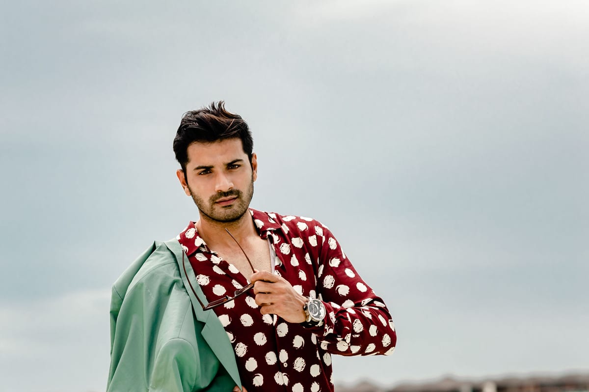 Fashionable portrait of a man on a Maldives beach in a polka dot shirt holding sunglasses.