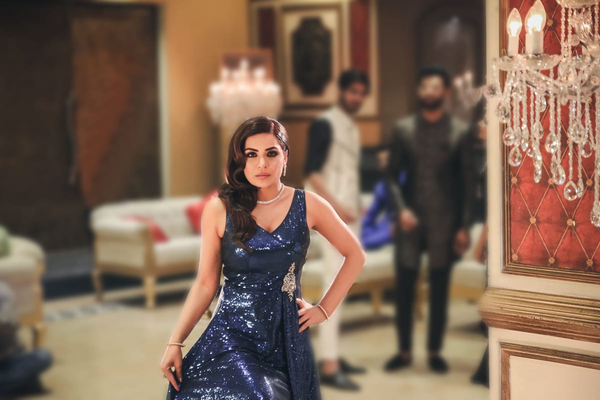 A stylish woman in a blue gown poses elegantly at a luxurious indoor event.