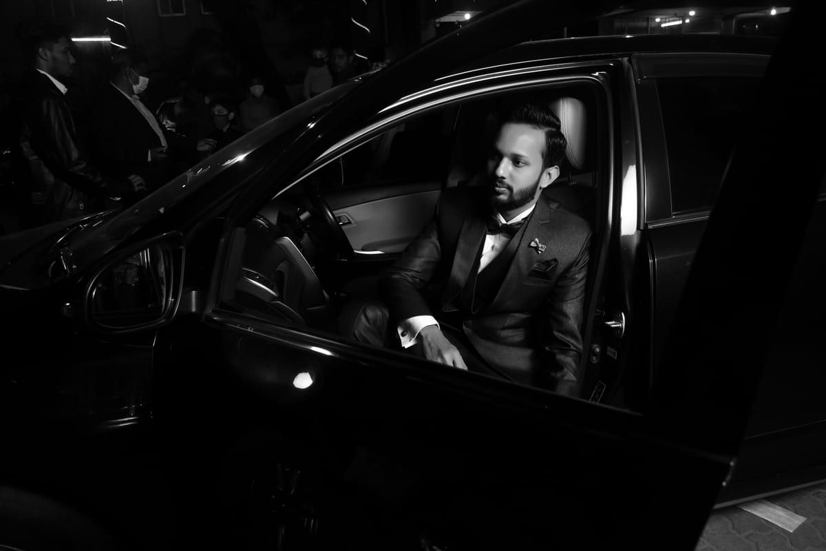 A well-dressed man in a tuxedo exits a stylish car under night lights, creating a sophisticated atmosphere.