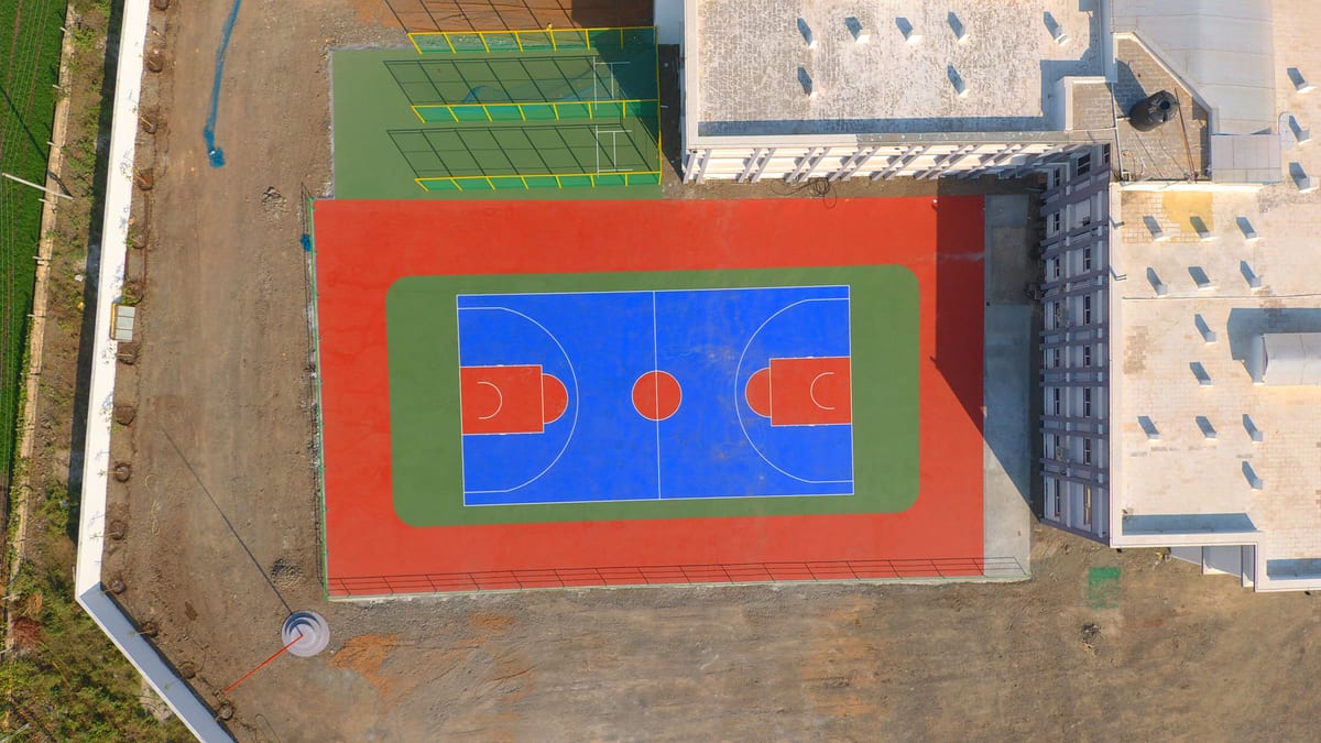 Aerial shot of vibrant basketball and tennis courts in Jamnagar, India, with distinct colors and urban surroundings.