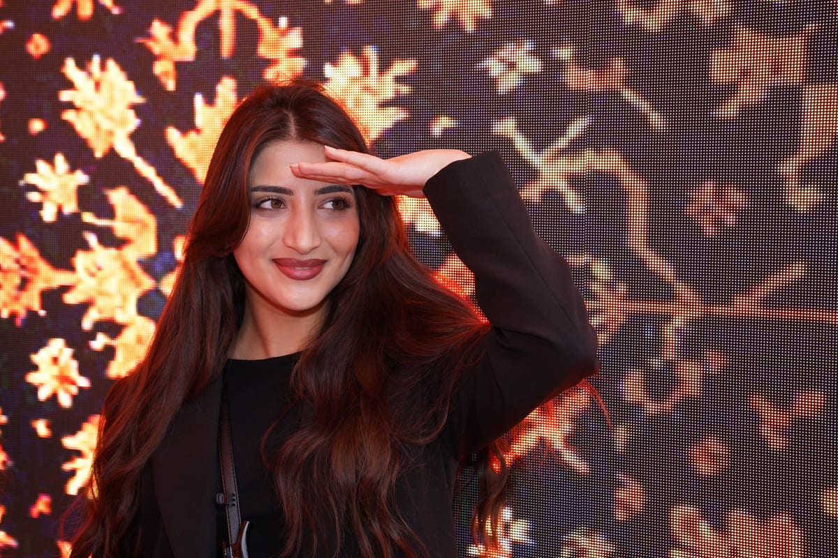 A smiling woman with long hair saluting against a colorful patterned backdrop.