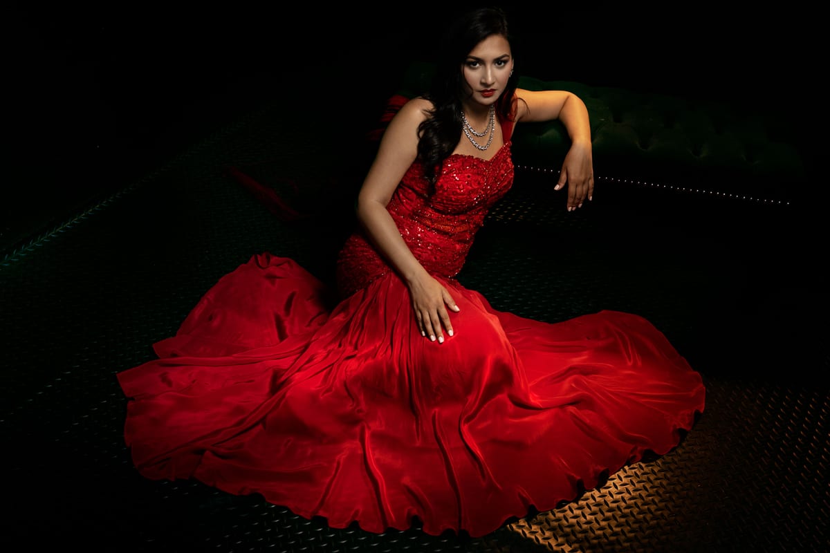 Captivating portrait of a woman in a red gown, exuding elegance and luxury against a dark backdrop.