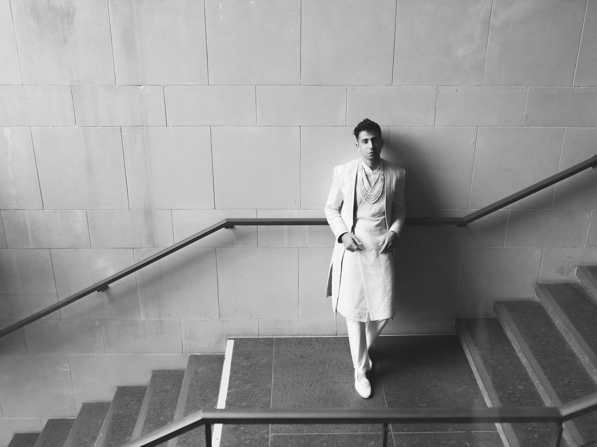 Monochrome portrait of a man in traditional attire leaning on a staircase indoors.