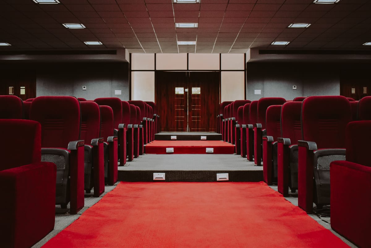 A luxurious empty auditorium with rows of red velvet seats and a red carpet aisle.