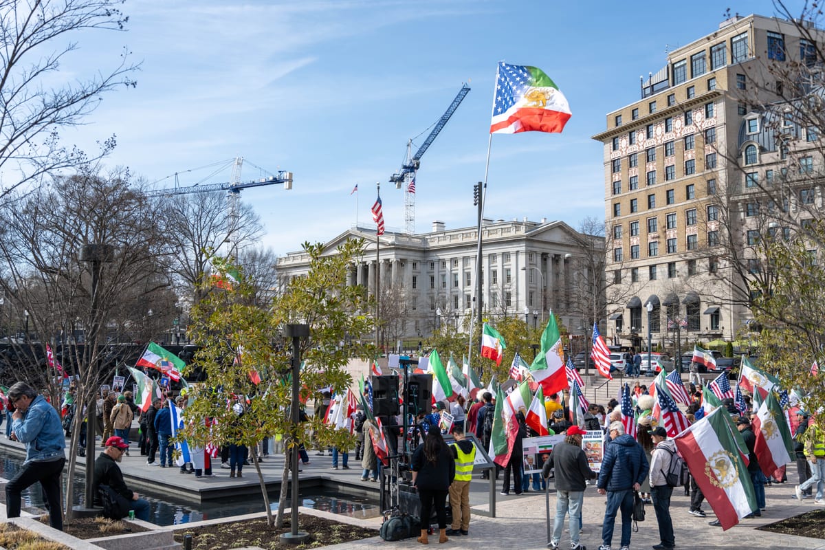 Crowd gathered in Washington D.C. protest holding flags with U.S. and other symbols outside government building.