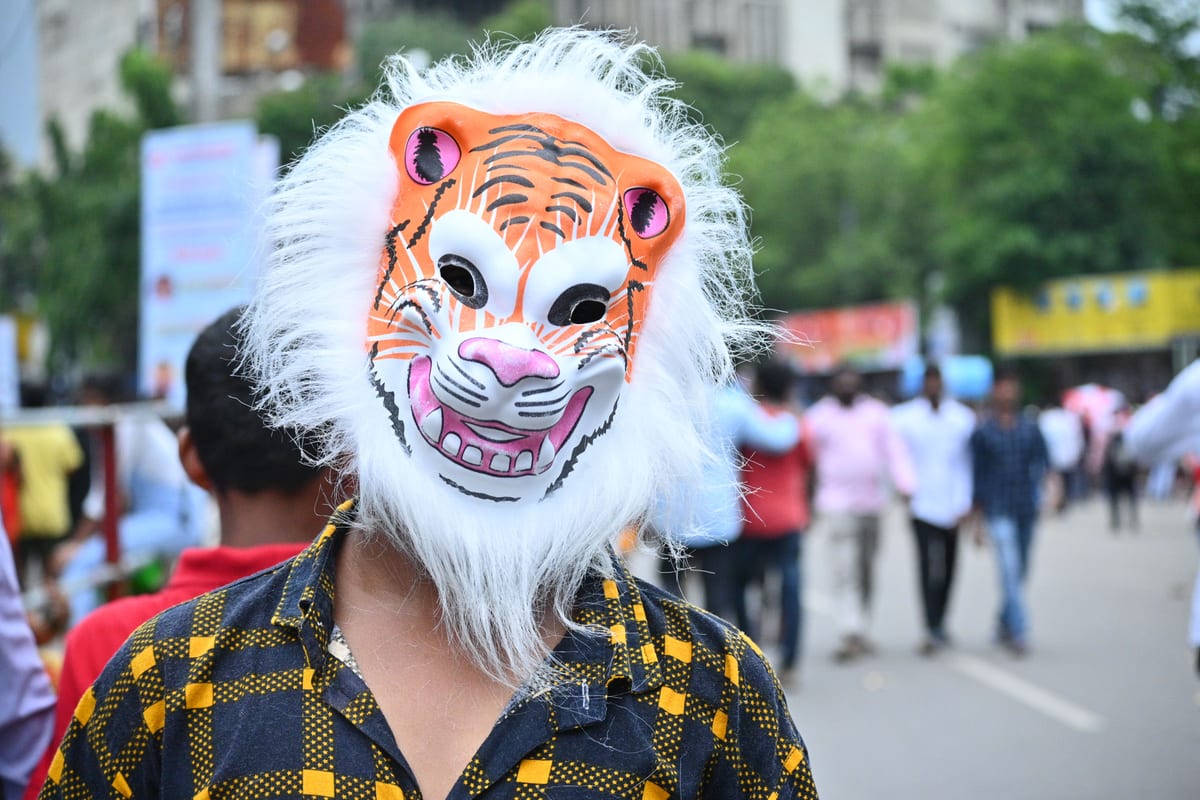A festive scene with a person wearing a vibrant tiger mask amidst a lively city street parade.