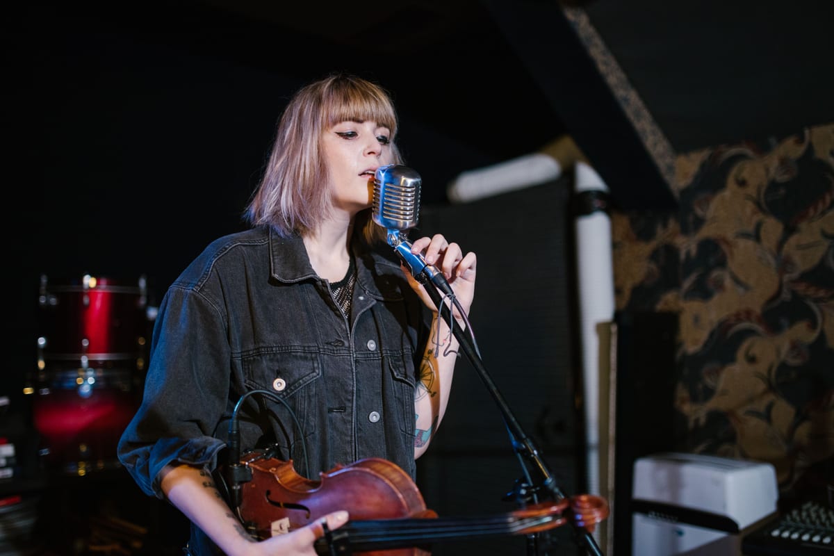 Woman singing while holding a violin on stage with a vintage microphone.