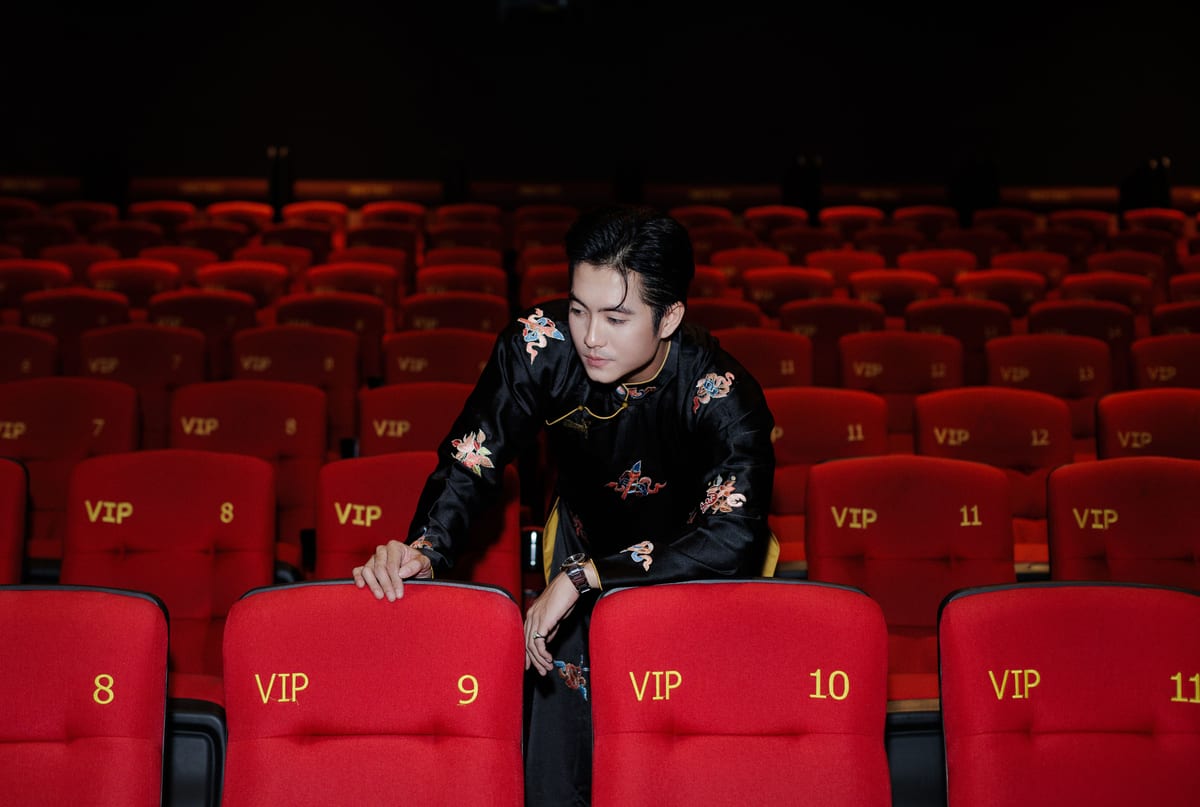 A person in a luxurious embroidered outfit in a VIP theater with empty red seats.