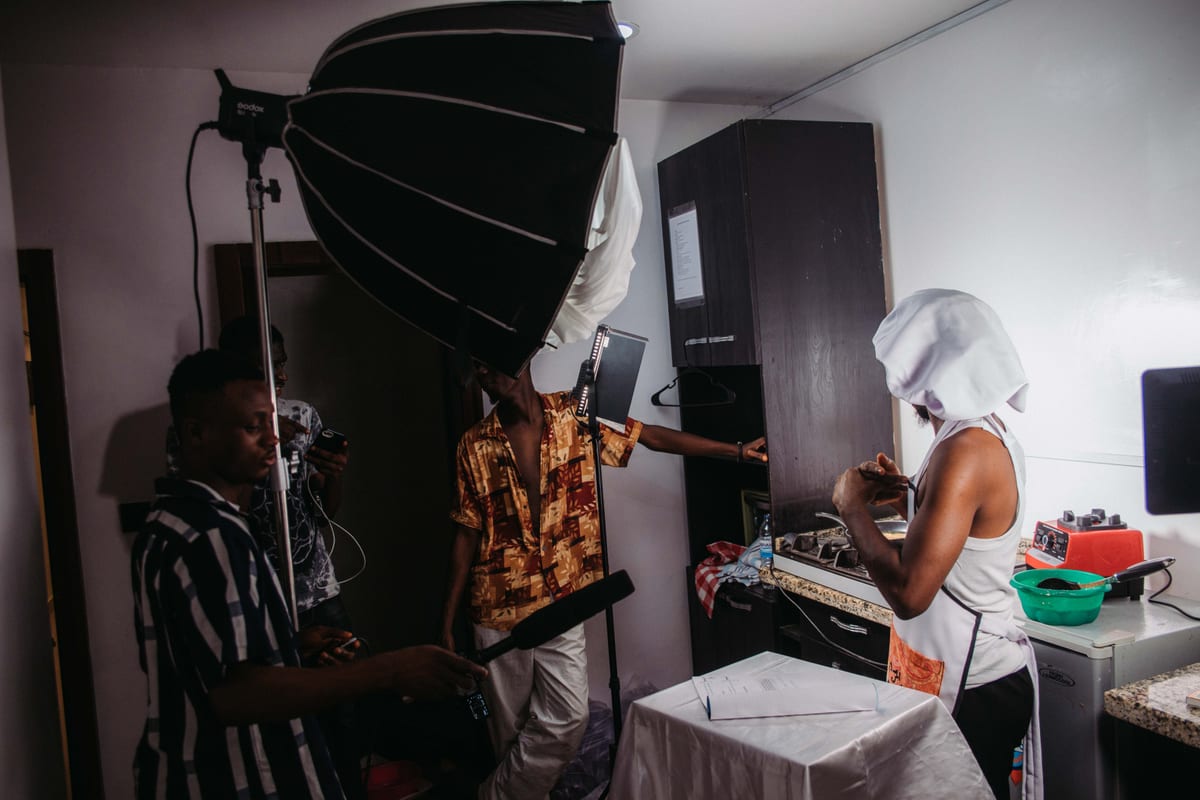 A filming crew records a cooking scene in a kitchen, featuring lighting and sound equipment.