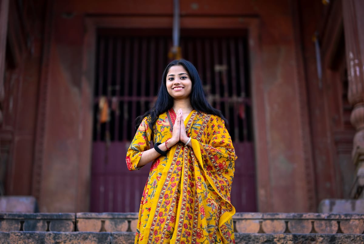 Happy woman wearing Indian sari greeting with Namaste gesture at a temple entrance in Varanasi.