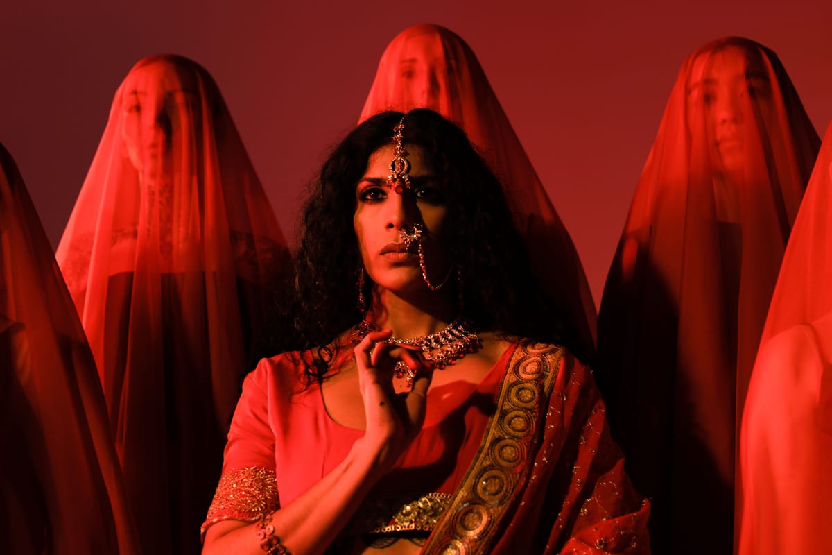 Striking portrait of an Indian woman in vibrant red sari and jewelry, surrounded by veiled figures.