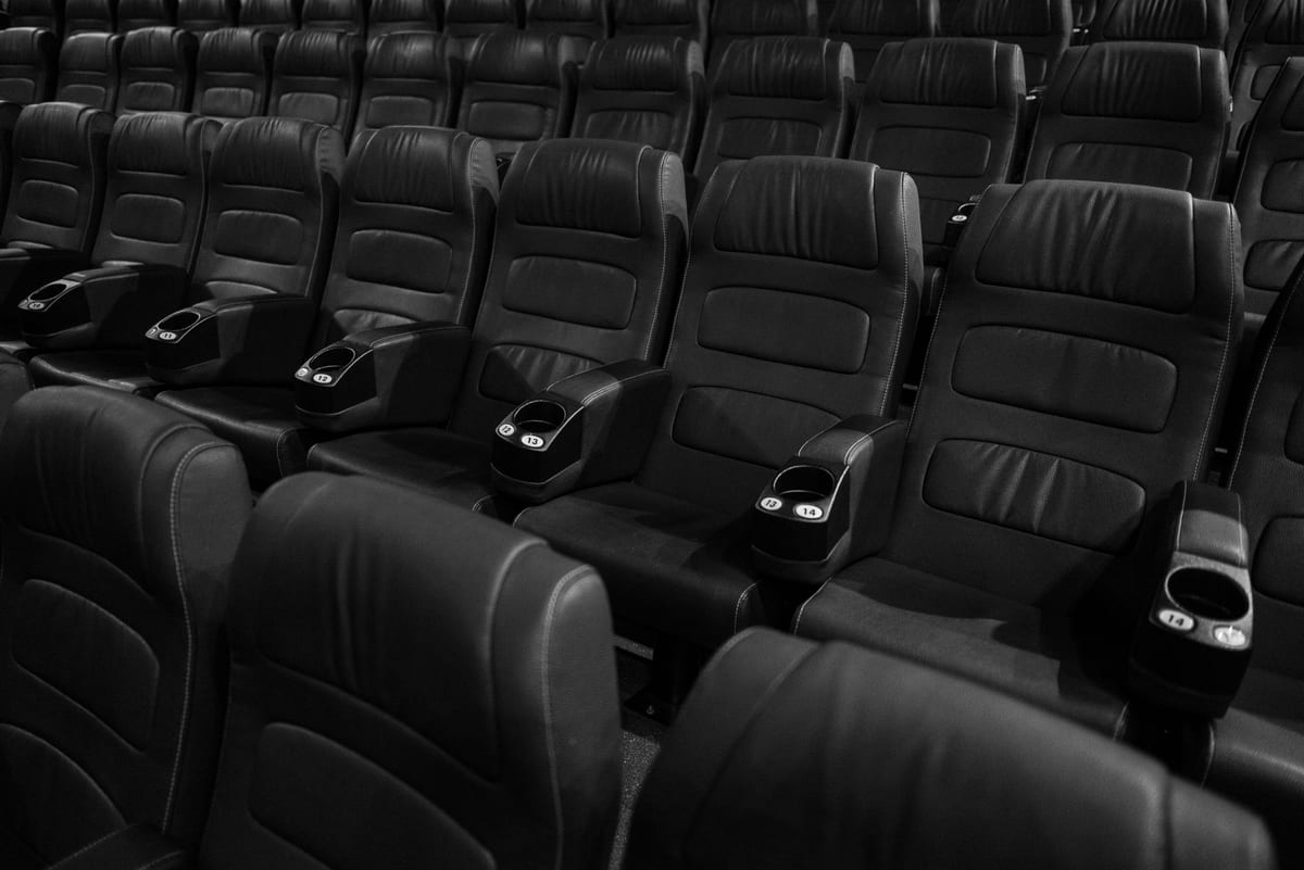Black and white image of empty leather seats in an indoor movie theater.