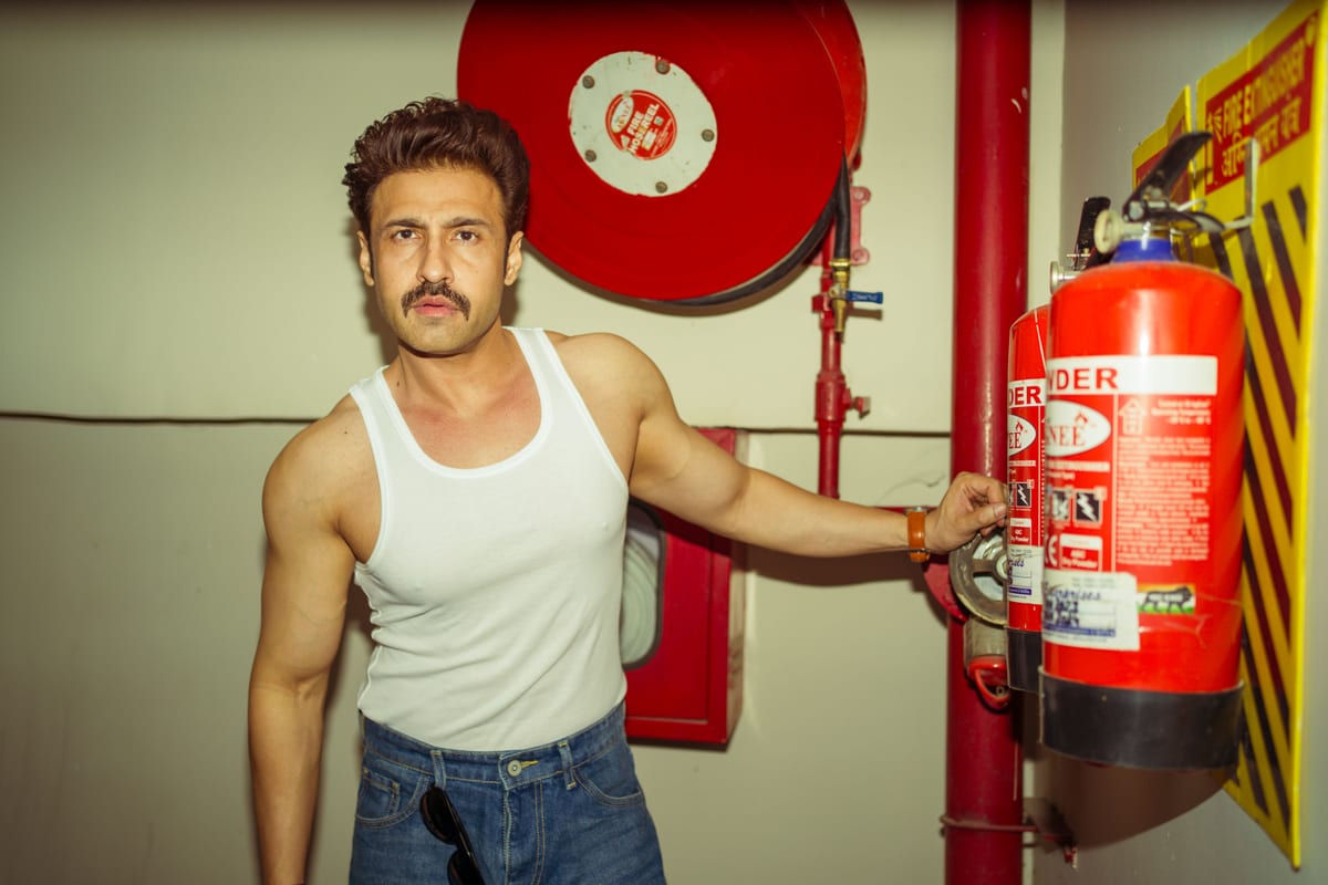 A confident man in a tank top poses with a fire extinguisher in an indoor setting.