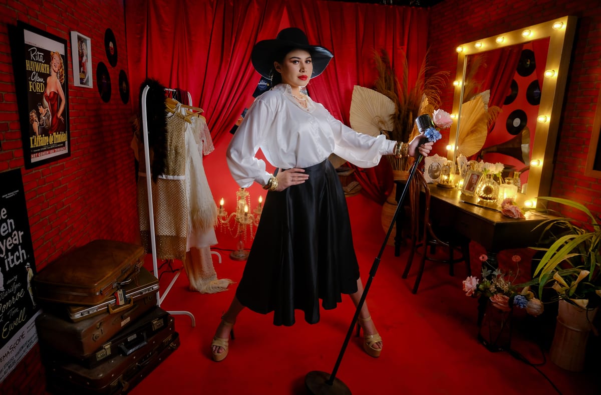 Elegant performer in vintage cabaret set with red curtains and vanity mirror.