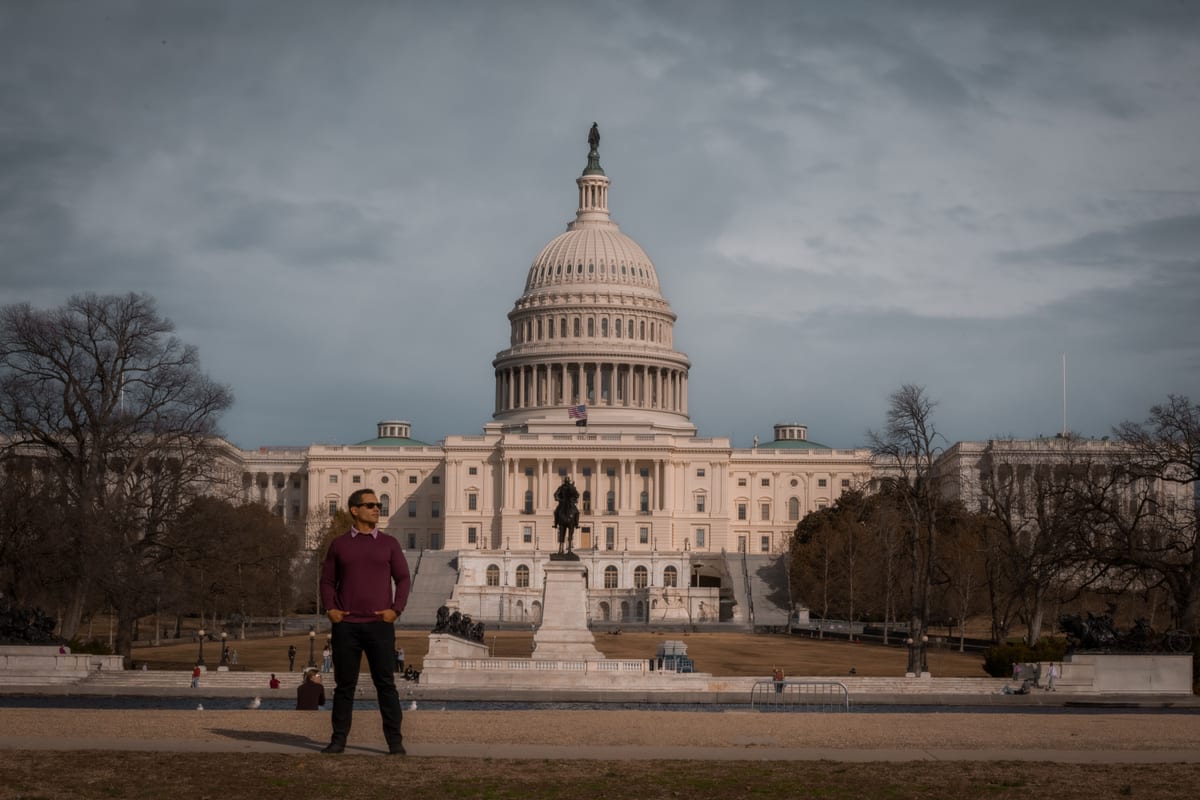 Person standing in front of the iconic United States Capitol on a clear day.