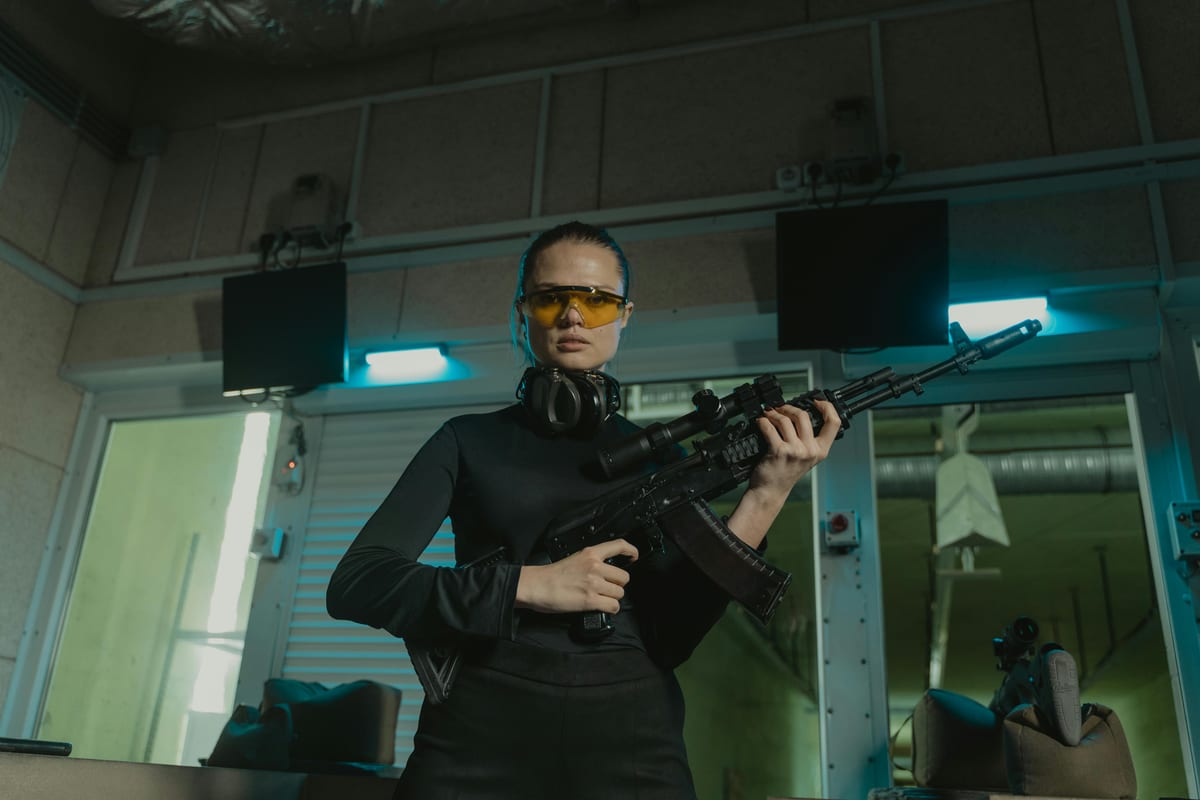 Confident woman wearing safety gear holding rifle at indoor shooting range.