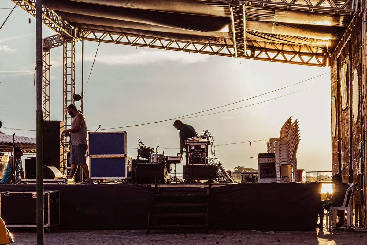 Musicians preparing outdoor stage during sunset with equipment and instruments.