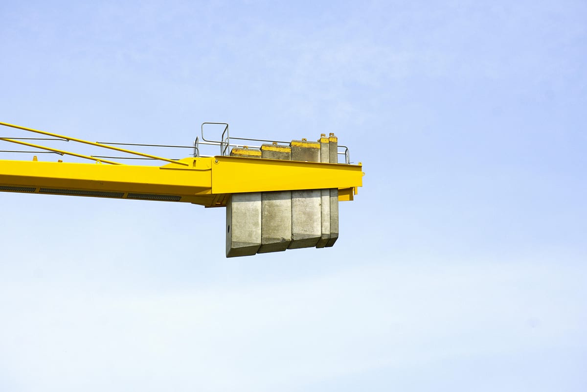 Close-up of a yellow construction crane arm with weights against a clear blue sky.