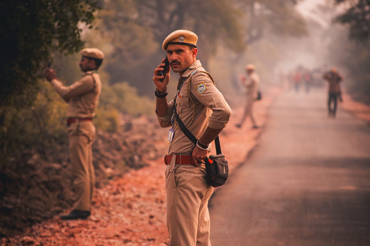 Indian police officer using phone on a rural road with colleagues.