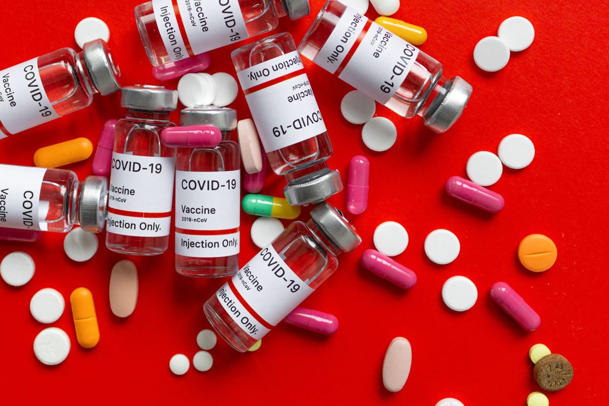 Top view of COVID-19 vaccine vials and various pills on a vibrant red background.
