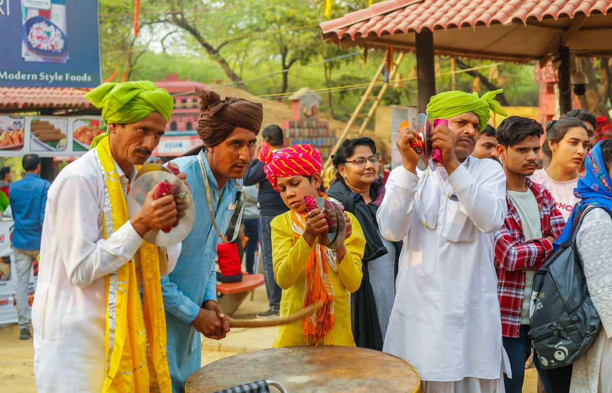 Indian men playing traditional music during a lively festival celebration outdoors.